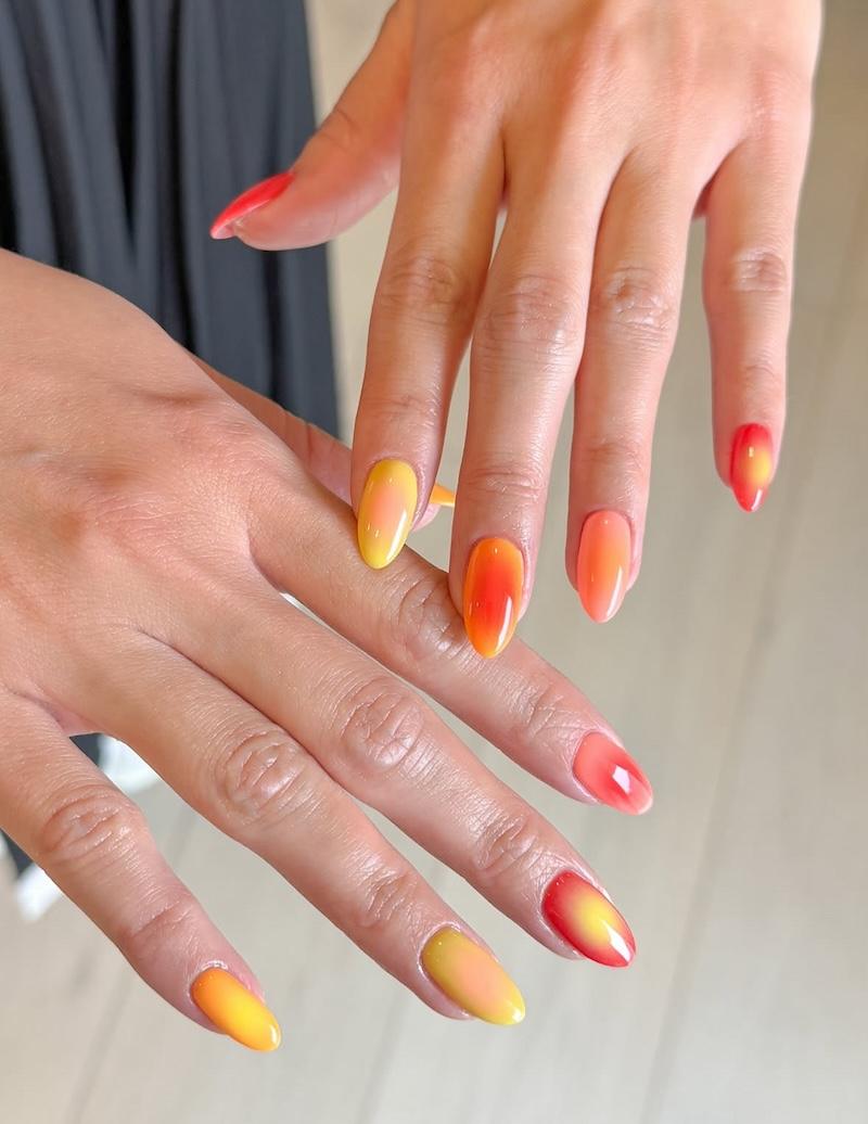 Diseño de uñas color naranja mango para el verano de estilo aura nails.