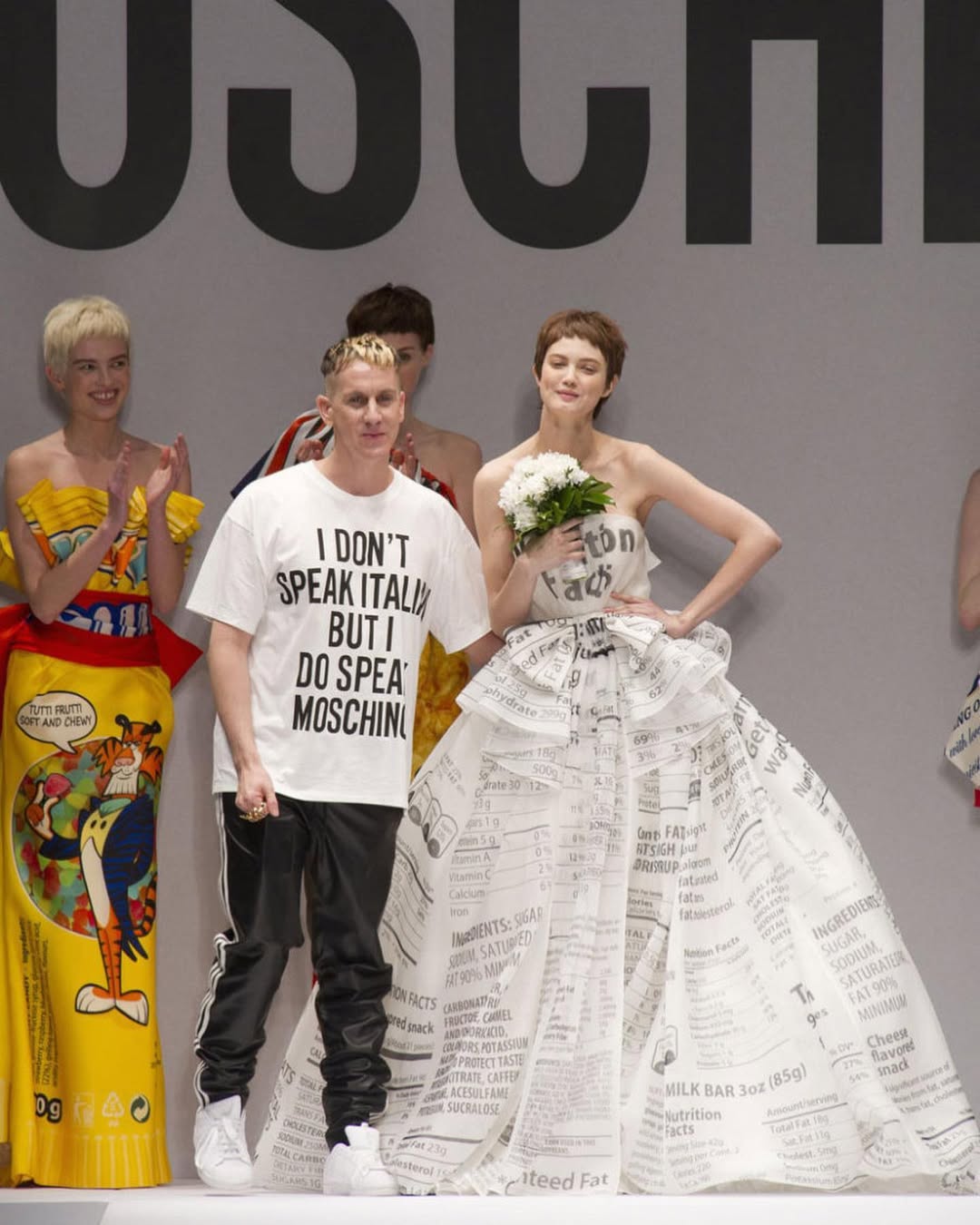 Jeremy Scott saluda al final de un desfile de Moschino junto a algunos de los diseños más icónicos de su etapa, marcada por el humor, la cultura pop y la estética del consumo. Imagen: @enfnsterribles