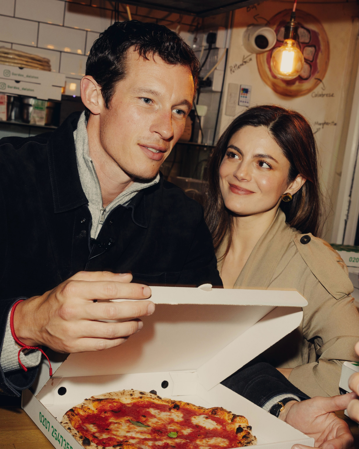 Callum Turner y Monica Barbaro juntos en un restaurante durante el rodaje de «Una noche al año» con una caja de pizza