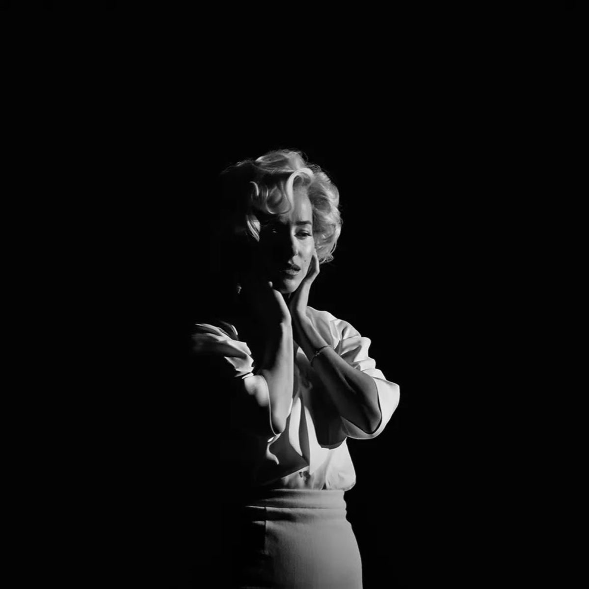 Dakota Johnson, como Marilyn Monroe, posa en una foto en blanco y negro con las manos sobre el rostro frente a un fondo negro