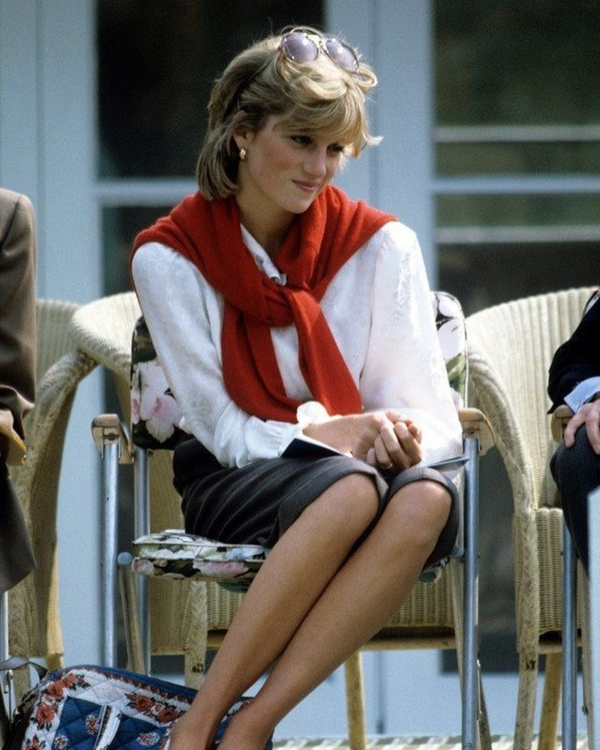 Diana de Gales sentada, con camisa blanca y jersey rojo sobre los hombros, luciendo un estilismo de inspiración «preppy»