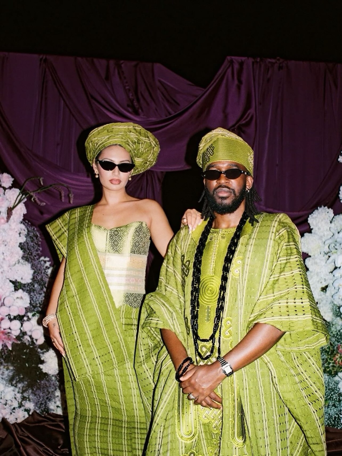 Pareja luciendo trajes tradicionales nigerianos de alta costura confeccionados en tejido Aso Oke de tonos verde oliva con detalles geométricos y accesorios a juego