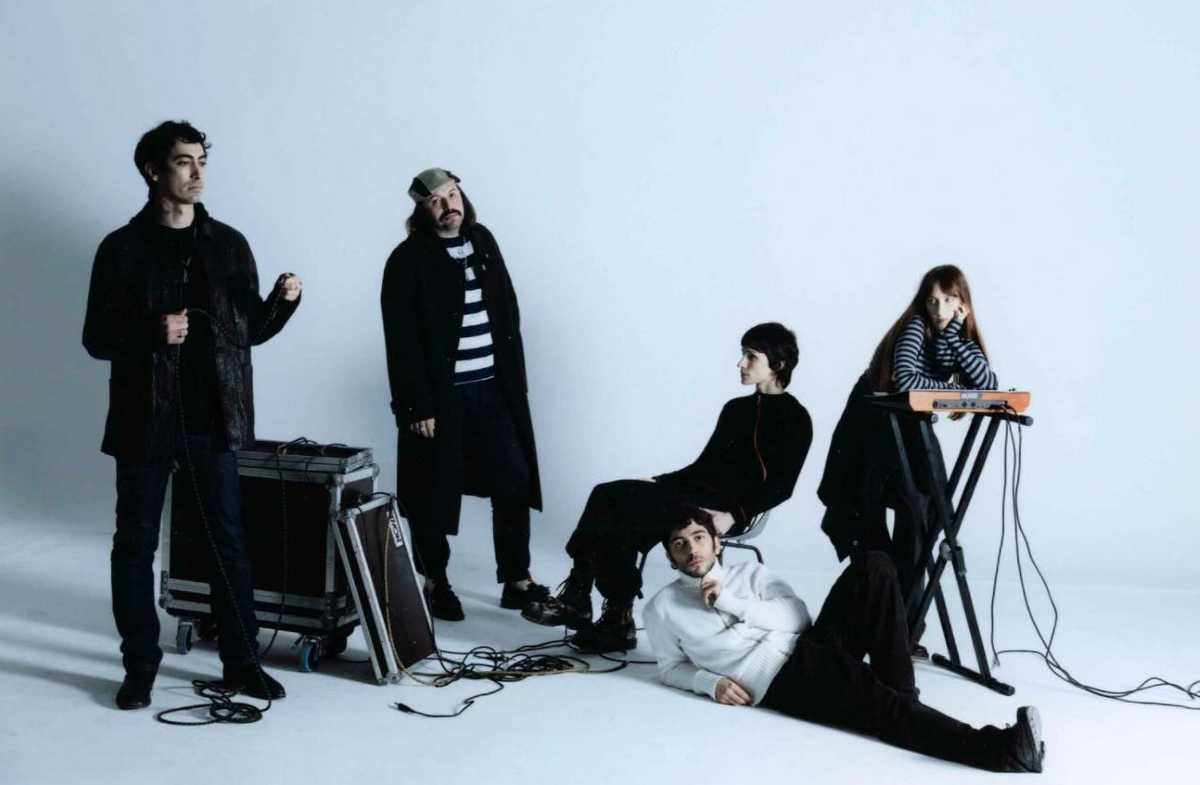 Los cinco integrantes de La Plata posan en un estudio de fondo blanco junto a instrumentos musicales y equipos de sonido, en una imagen promocional de la banda