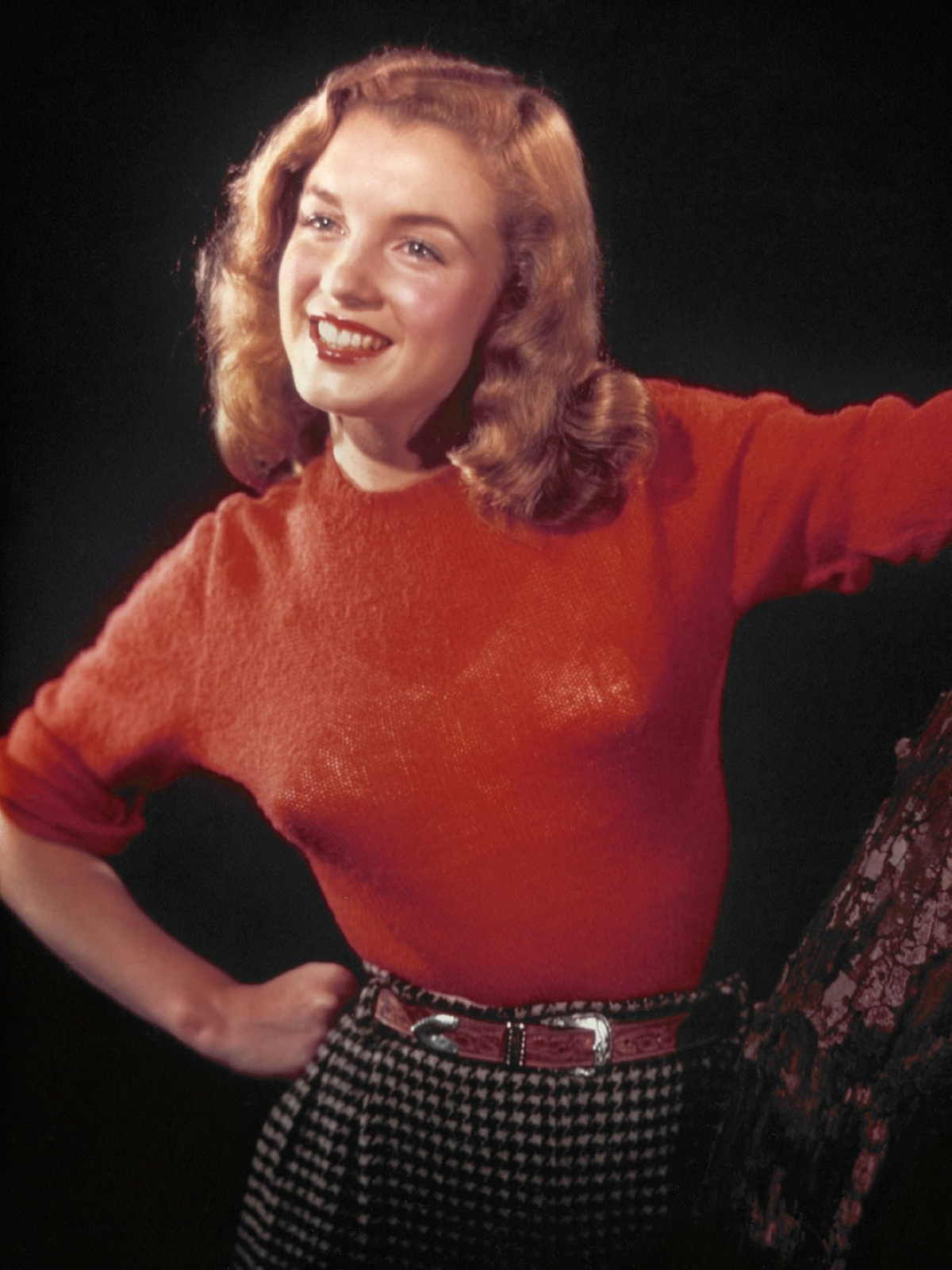 Norma Jeane posa sonriente con un jersey rojo y una falda de cuadros durante una sesión fotográfica de 1945, antes de adoptar el nombre artístico de Marilyn Monroe y comenzar su ascenso como estrella de Hollywood