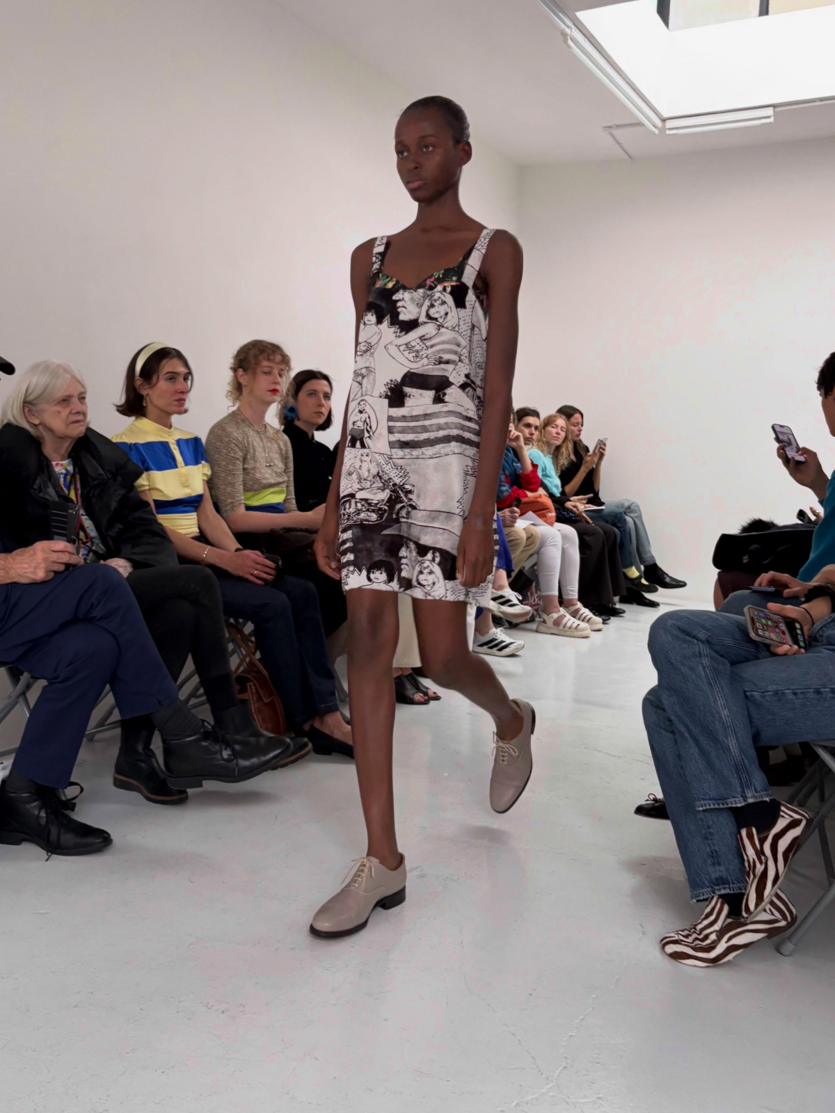 Modelo luce el look 23 de la colección primavera-verano 2027 de A Letter, inspirado en la estética de un periódico y combinado con zapatos realizados en colaboración con Grenson