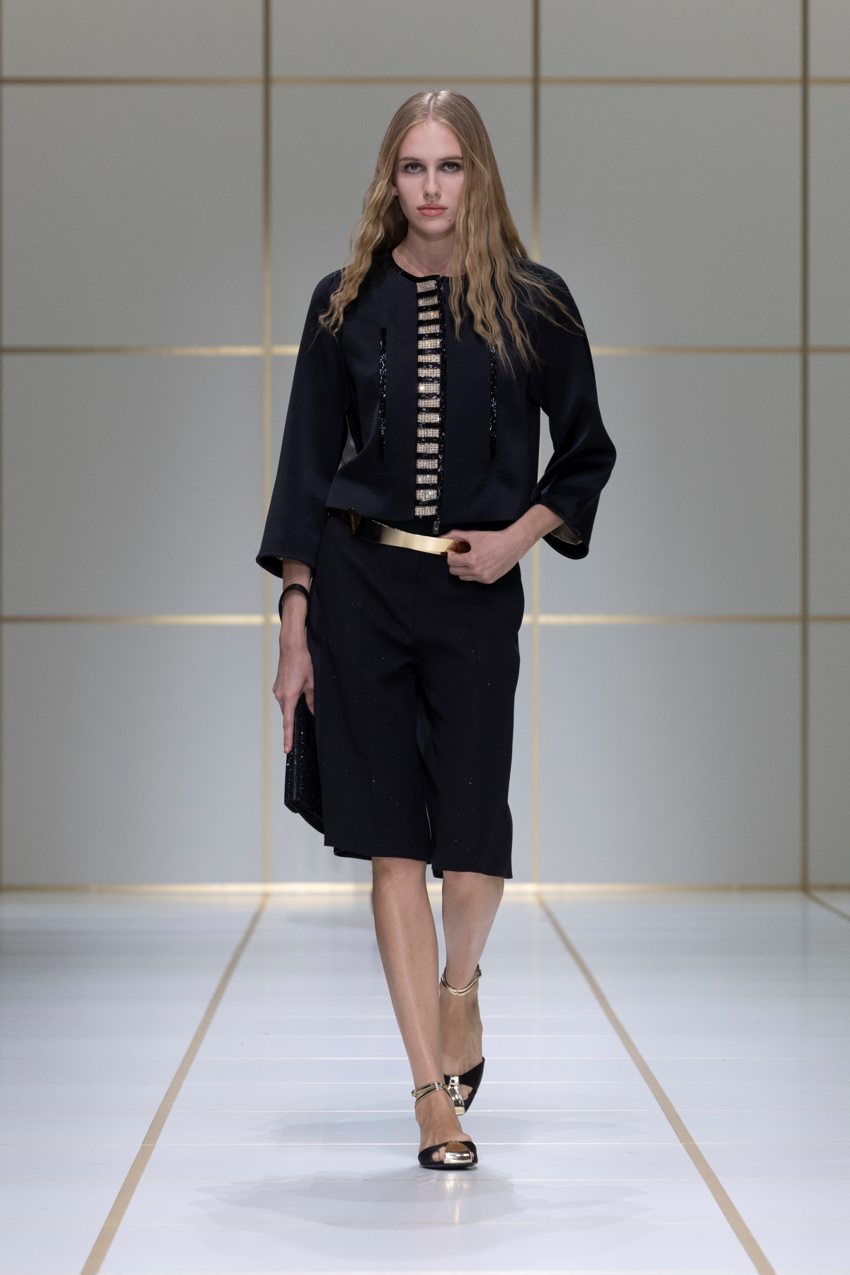 Look 47 de Giorgio Armani Primavera-Verano 2027, con top marfil asimétrico de acabado brillante, americana negra estructurada y broche dorado de mariposa