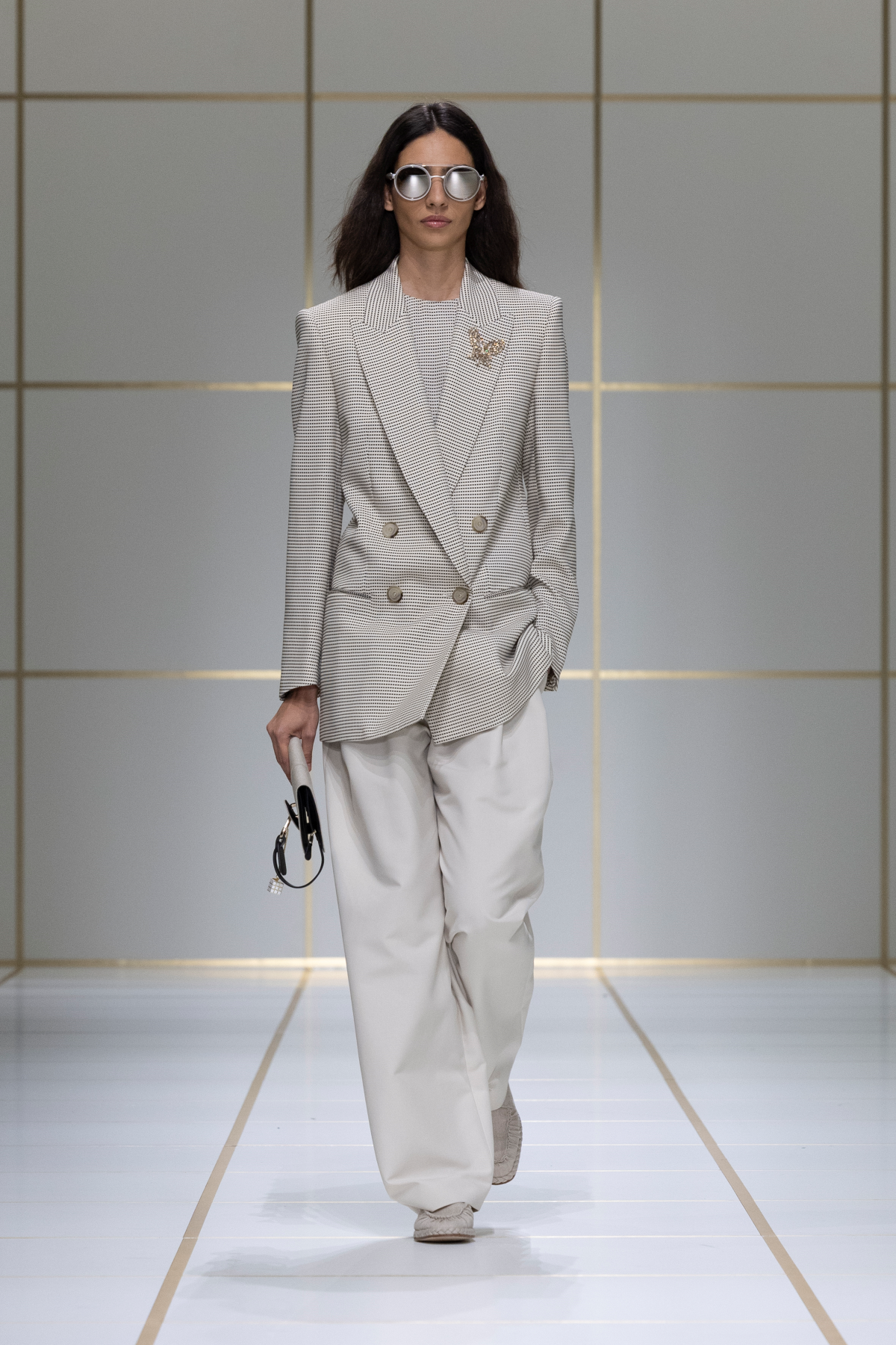 Look 1 de Giorgio Armani Primavera-Verano 2027 «EVOLUTION», con americana cruzada de doble botonadura en tono marfil, pantalón amplio, gafas de montura plateada, bolso negro y broche dorado