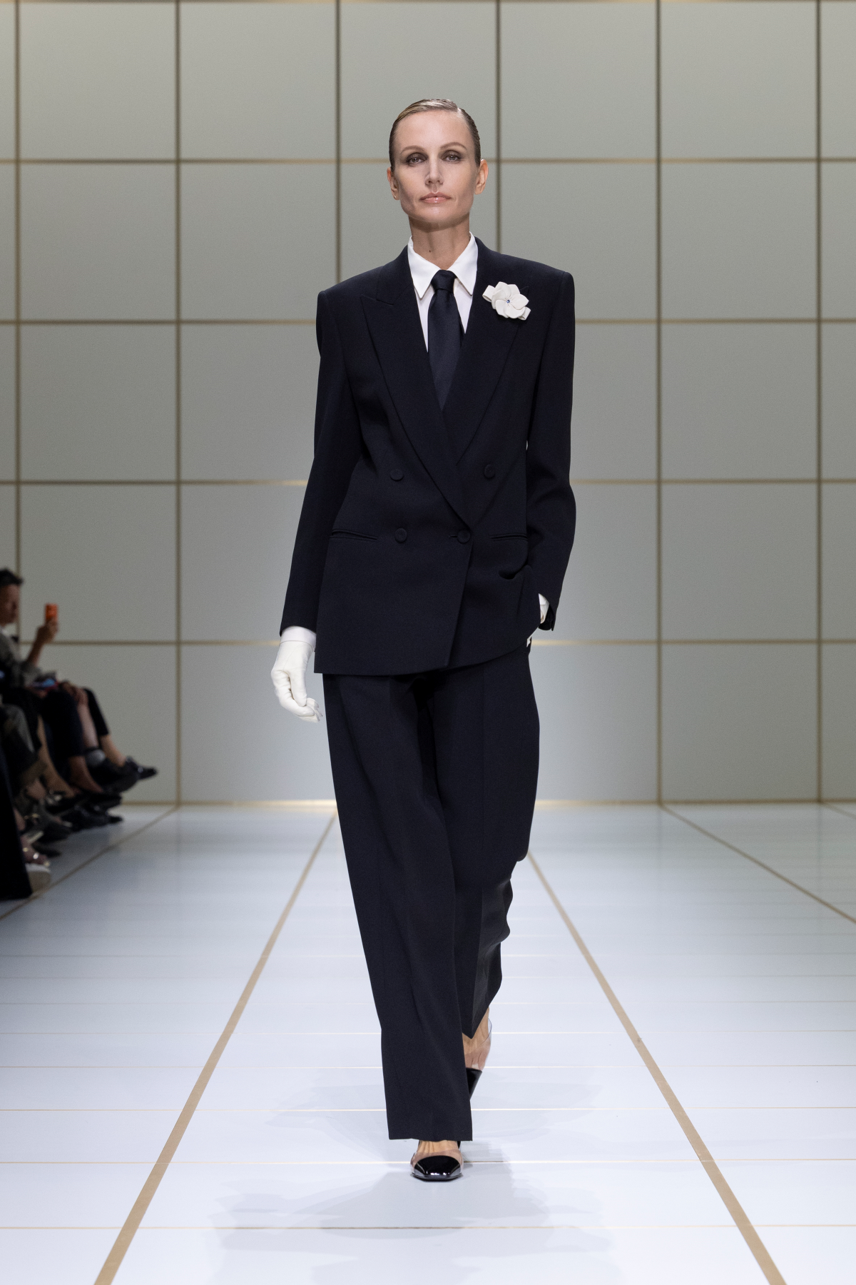 Look 22 de Giorgio Armani Primavera-Verano 2027, con esmoquin negro cruzado, camisa blanca, corbata negra, guantes blancos y detalle floral blanco en la solapa