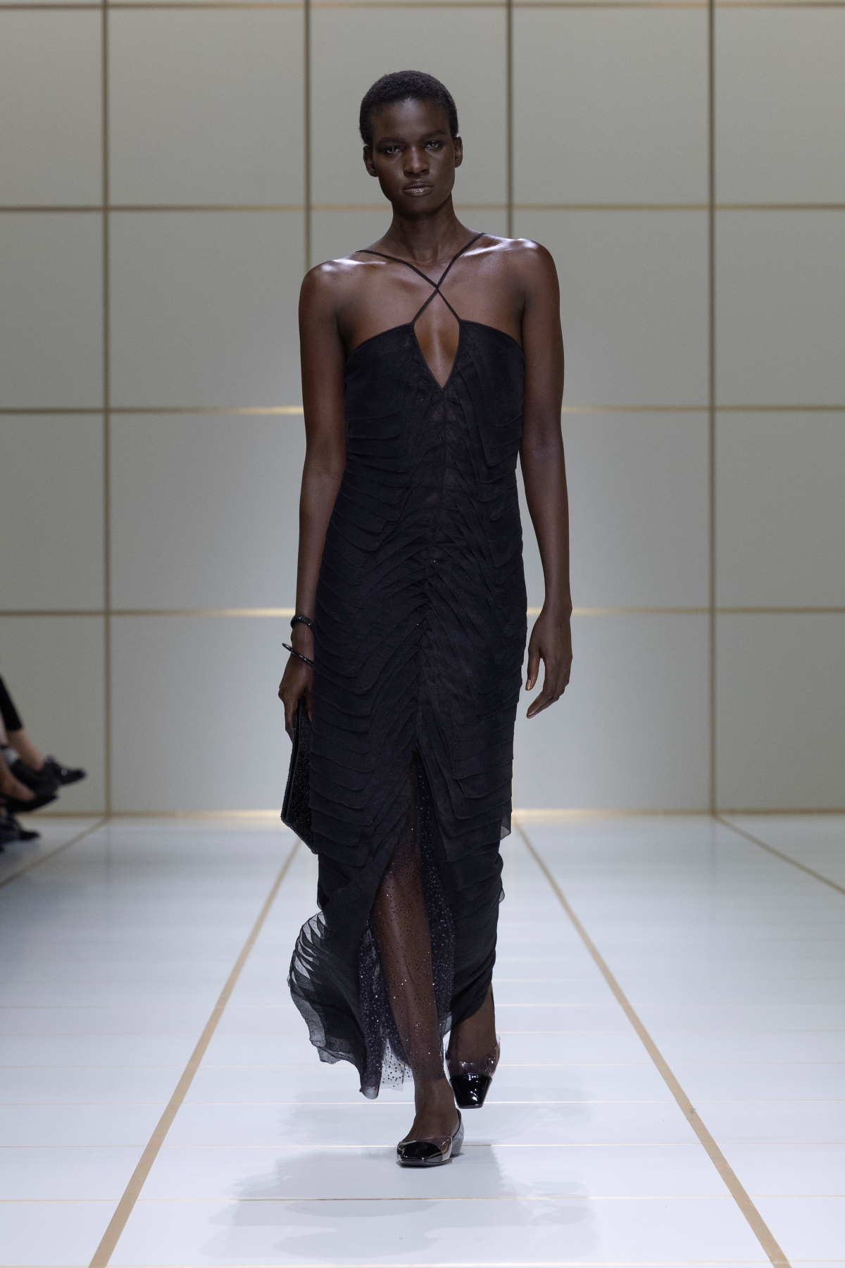 Look 45 de Giorgio Armani Primavera-Verano 2027 «EVOLUTION», con vestido negro de silueta fluida, cuerpo semitransparente con detalles dorados, bolso pequeño negro y zapatos planos