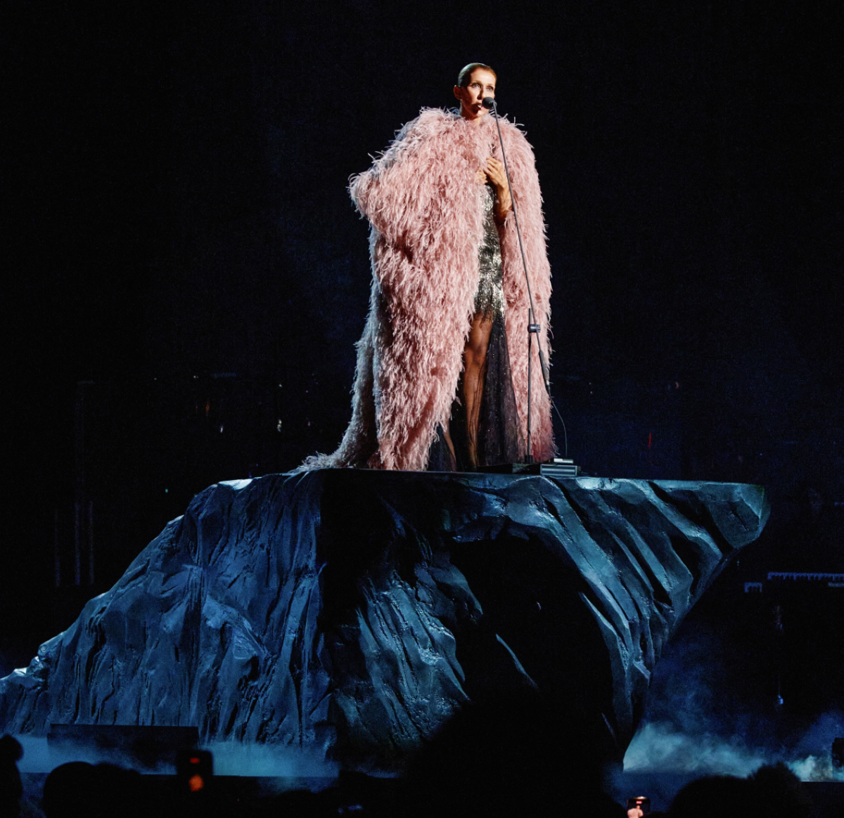 Céline Dion sobre el escenario con un look de Givenchy formado por un vestido negro bordado con aberturas, salones negros de punta y una capa de organza rosa empolvado con acabado desgarrado