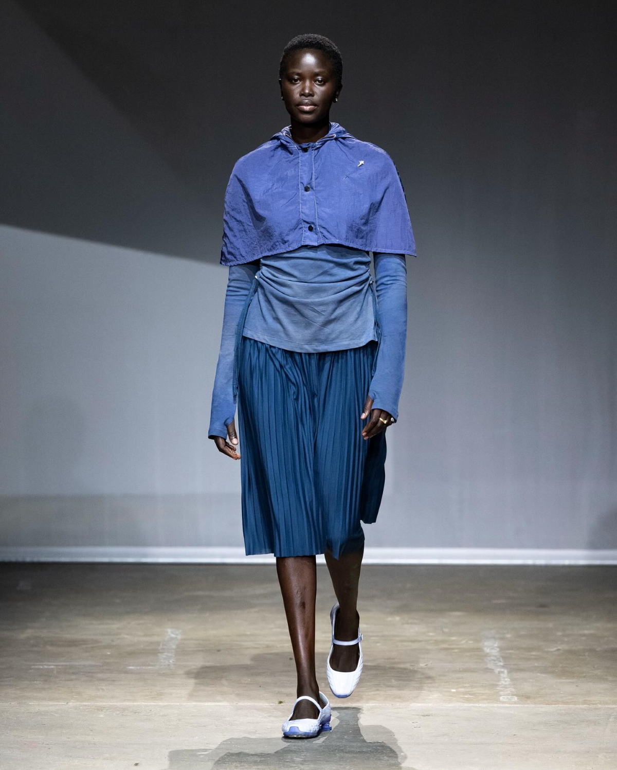 La modelo Mimi luce el look 9 de la Season 7 de Charlie Constantinou, formado por un vestido de jersey plisado con polo de ajuste regulable, un poncho corto de nailon y unas Nike Shox Callistra teñidas