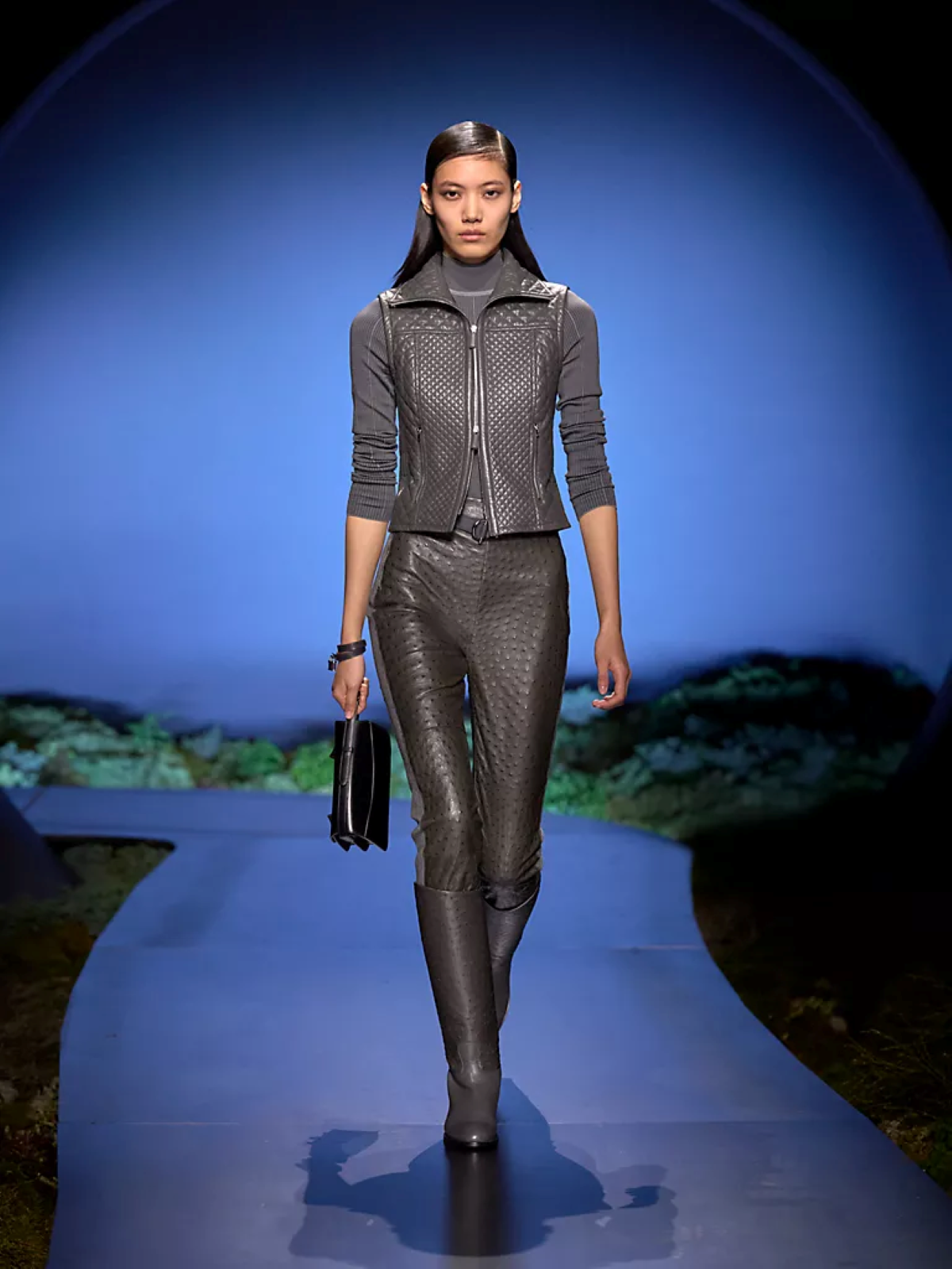 Modelo con chaleco de piel gris, pantalón ajustado de piel y botas altas por encima de la rodilla, durante el desfile de Hermès otoño-invierno 2026