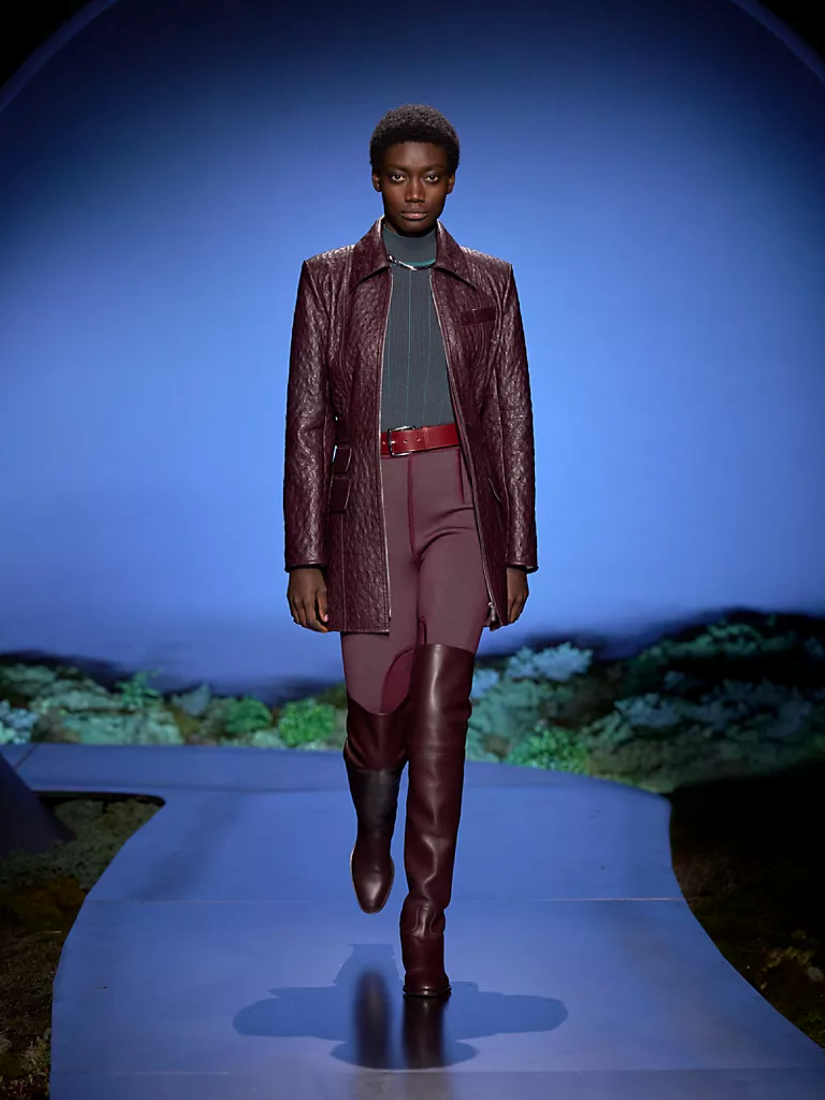 Look 17 de Hermès otoño-invierno 2026 con chaqueta y pantalón jodhpur en tono burdeos, combinado con botas altas de inspiración ecuestre