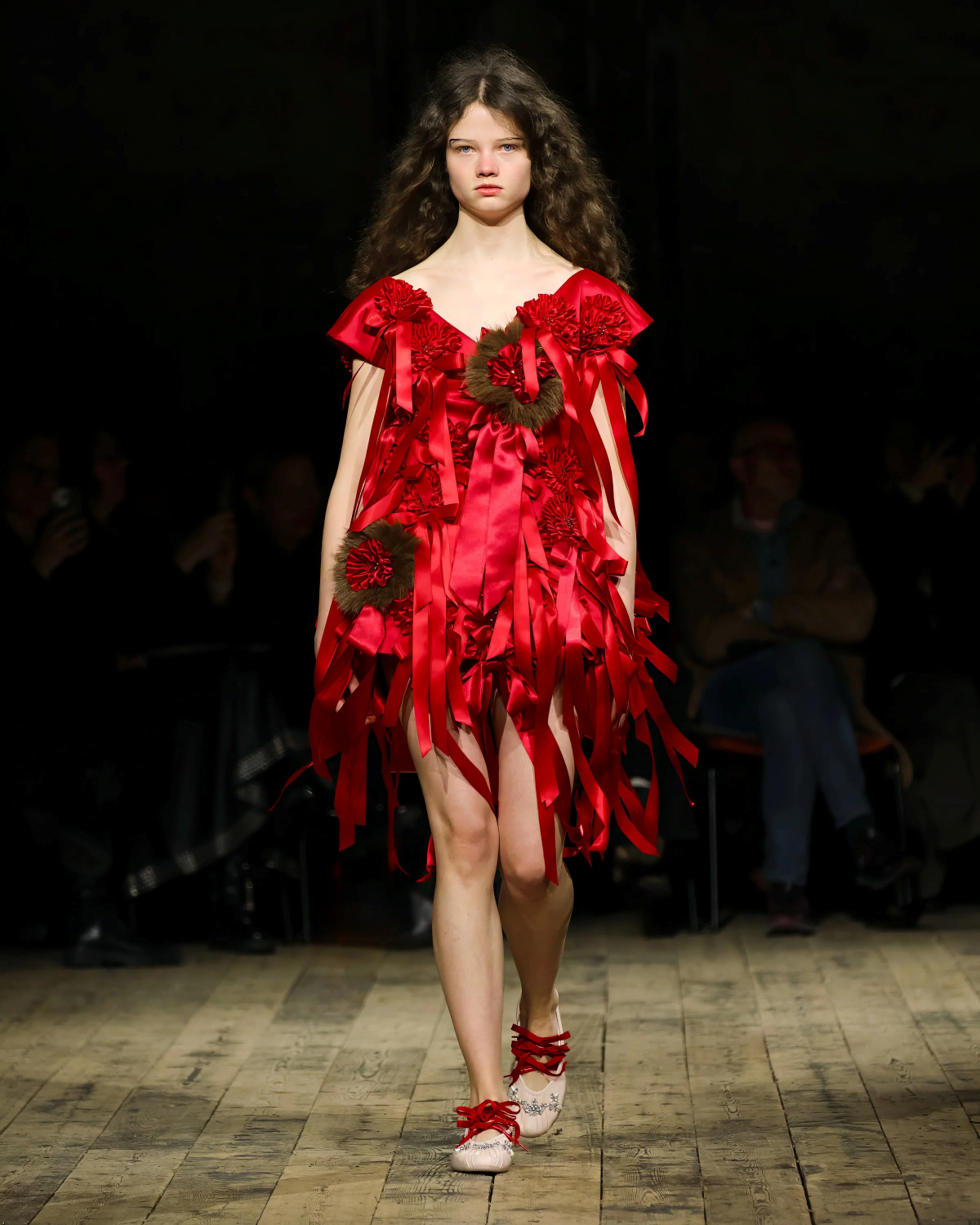 Look 27 de Simone Rocha FW26 con vestido corto rojo decorado con numerosas rosetas, cintas y medallas, combinado con bailarinas a juego