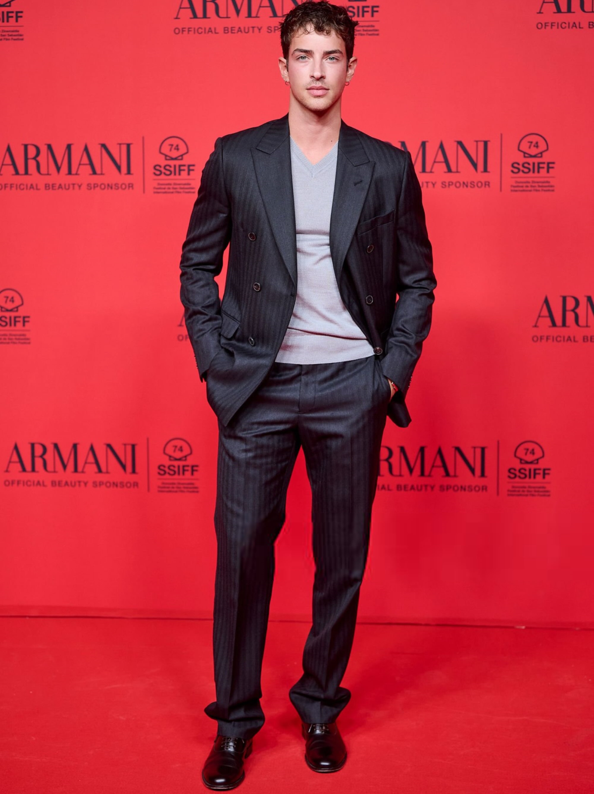 Manu Ríos posa con un traje negro de Emporio Armani y un jersey gris durante el Festival de San Sebastián