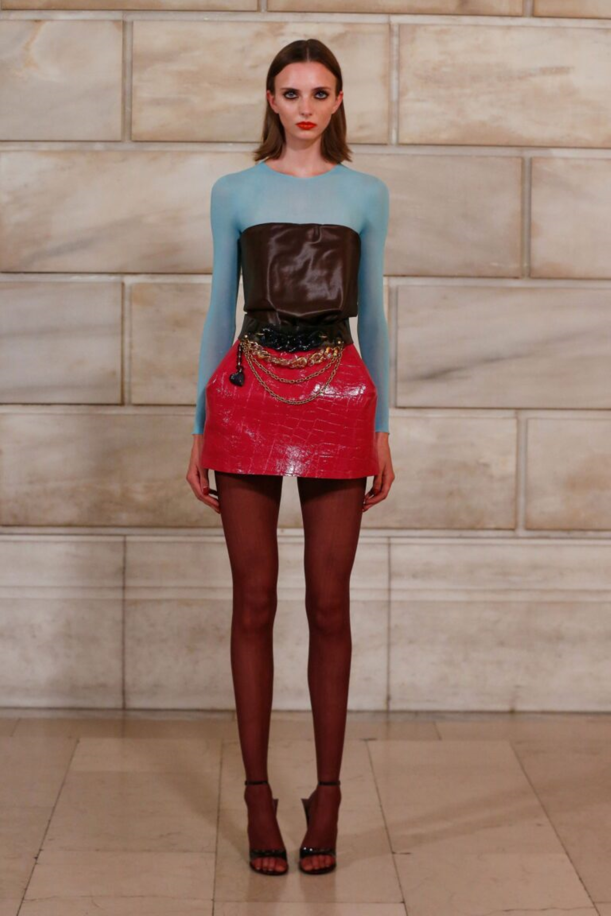Look 8 de Marc Jacobs Primavera-Verano 2027 con top azul turquesa, mangas lavanda, minifalda ciruela efecto charol, medias naranjas y cinturones de cadena
