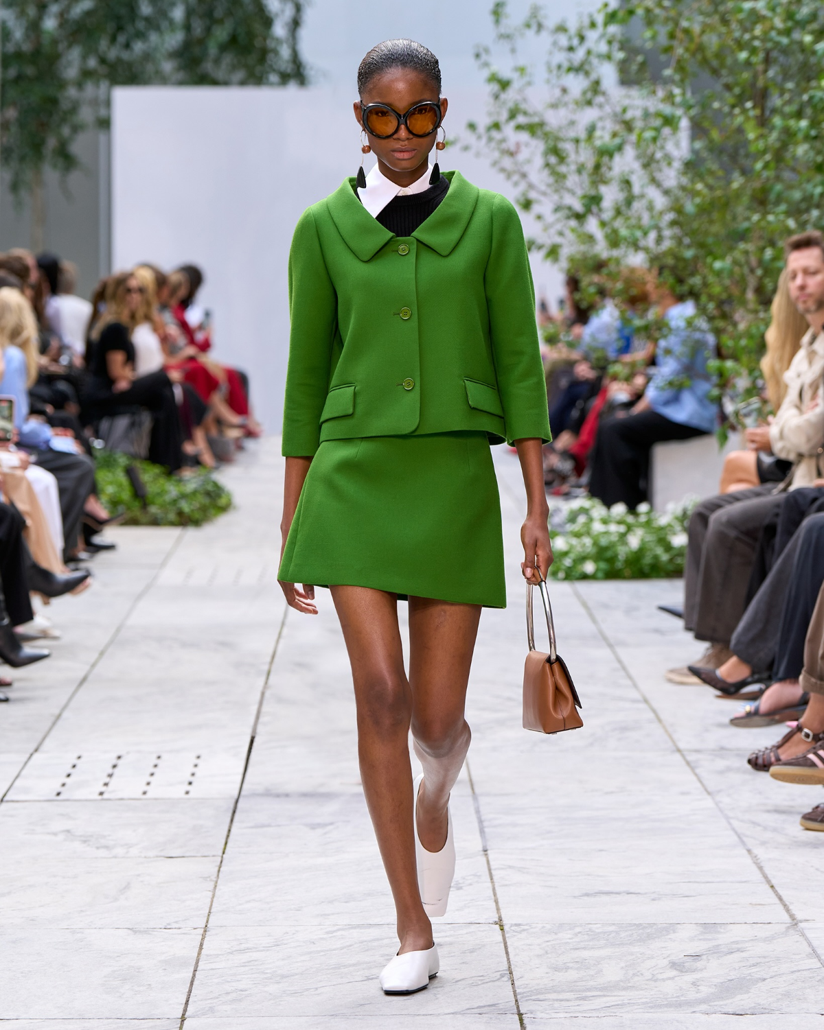 Look verde de MICHAEL KORS con minifalda, chaqueta corta, gafas bug-eye y zapatos blancos, inspirado en los años 60