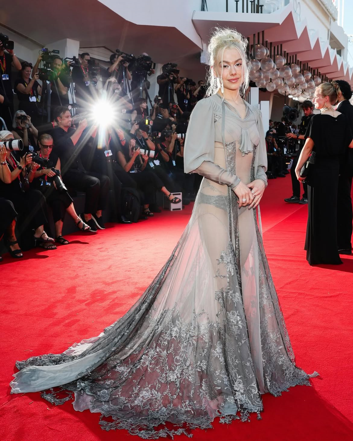 Phoebe Bridgers posa en la alfombra roja con un vestido gris de encaje floral semitransparente, con corpiño transparente, mangas largas de inspiración victoriana y larga cola, de Alexander McQueen.