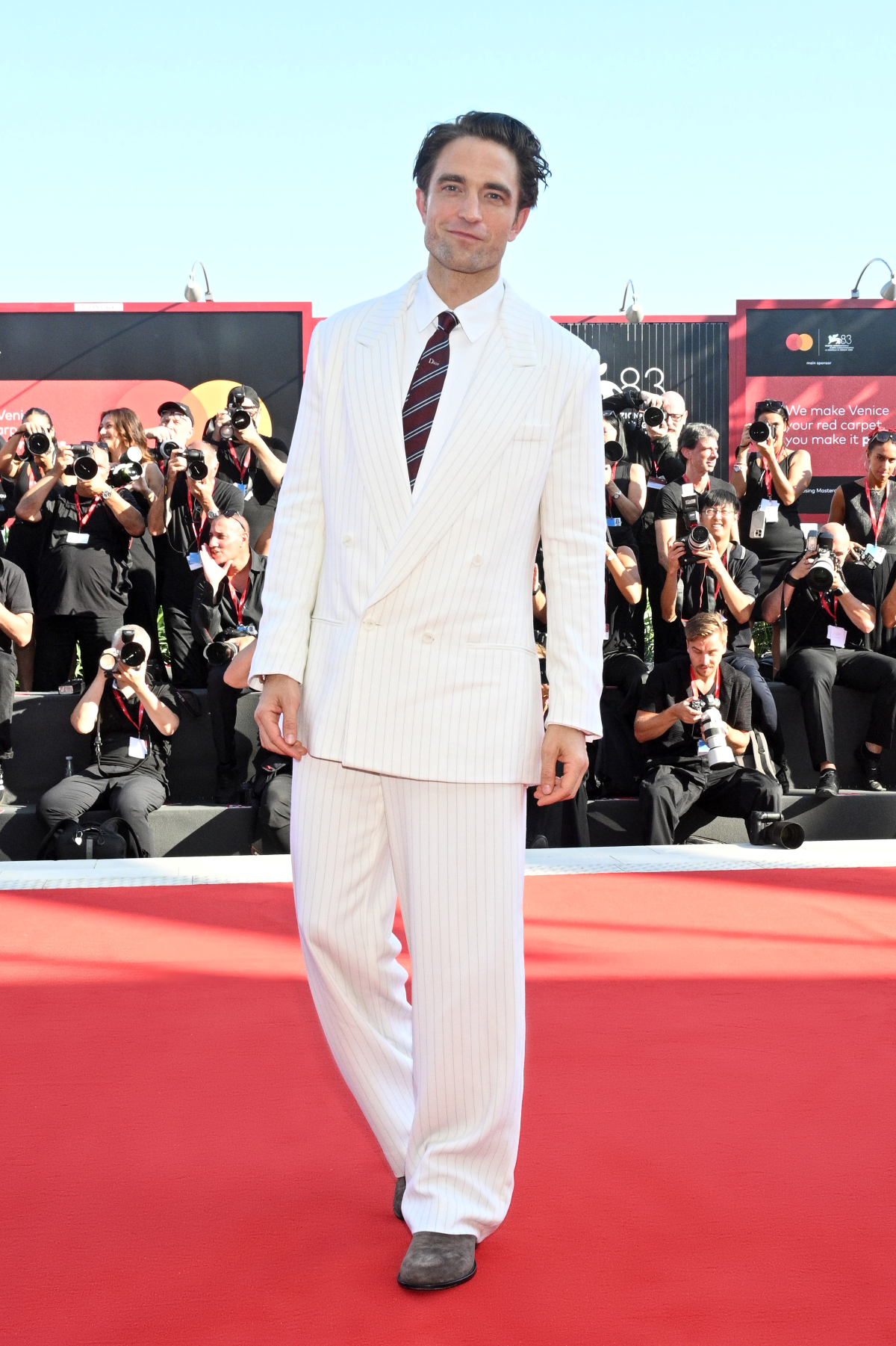 Robert Pattinson luce un traje cruzado de lana blanca a rayas con camisa blanca, corbata de seda roja a rayas y mocasines de ante marrón