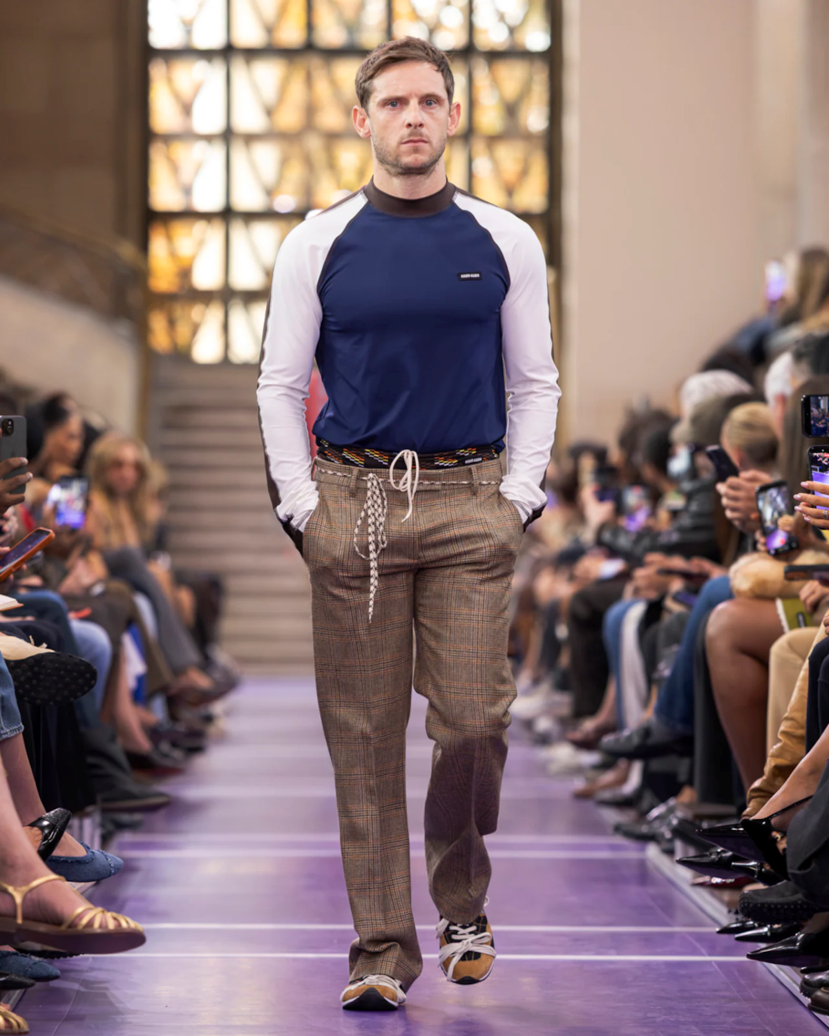 Jamie Bell desfila para Miu Miu Primavera-Verano 2027 con un top deportivo azul marino y blanco y pantalón de cuadros