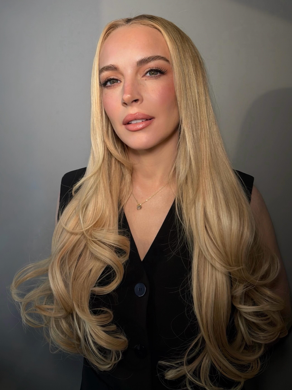 Lindsay Lohan con una melena larga, rubia y luminosa, peinada con ondas suaves y capas degradadas que enmarcan el rostro y aportan movimiento