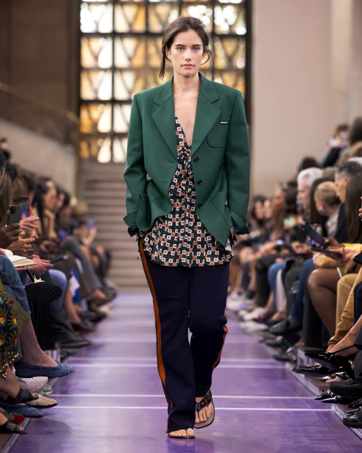 Ella Bleu Travolta desfila para Miu Miu Primavera/Verano 2027 con blazer verde caqui y top de estampado geométrico