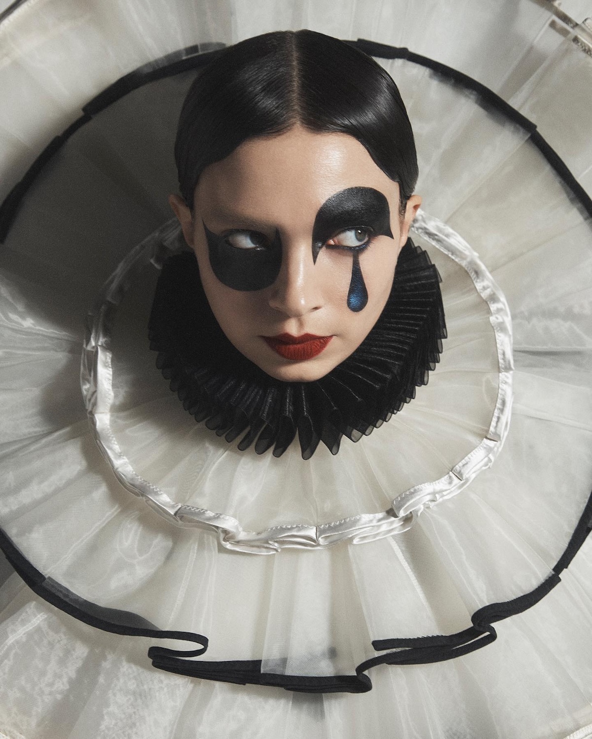La imagen muestra una fotografía de una persona con un maquillaje artístico inspirado en el personaje de Pierrot, con un volante de cuello plisado en blanco y negro. Imagen: @thegirlonthebike