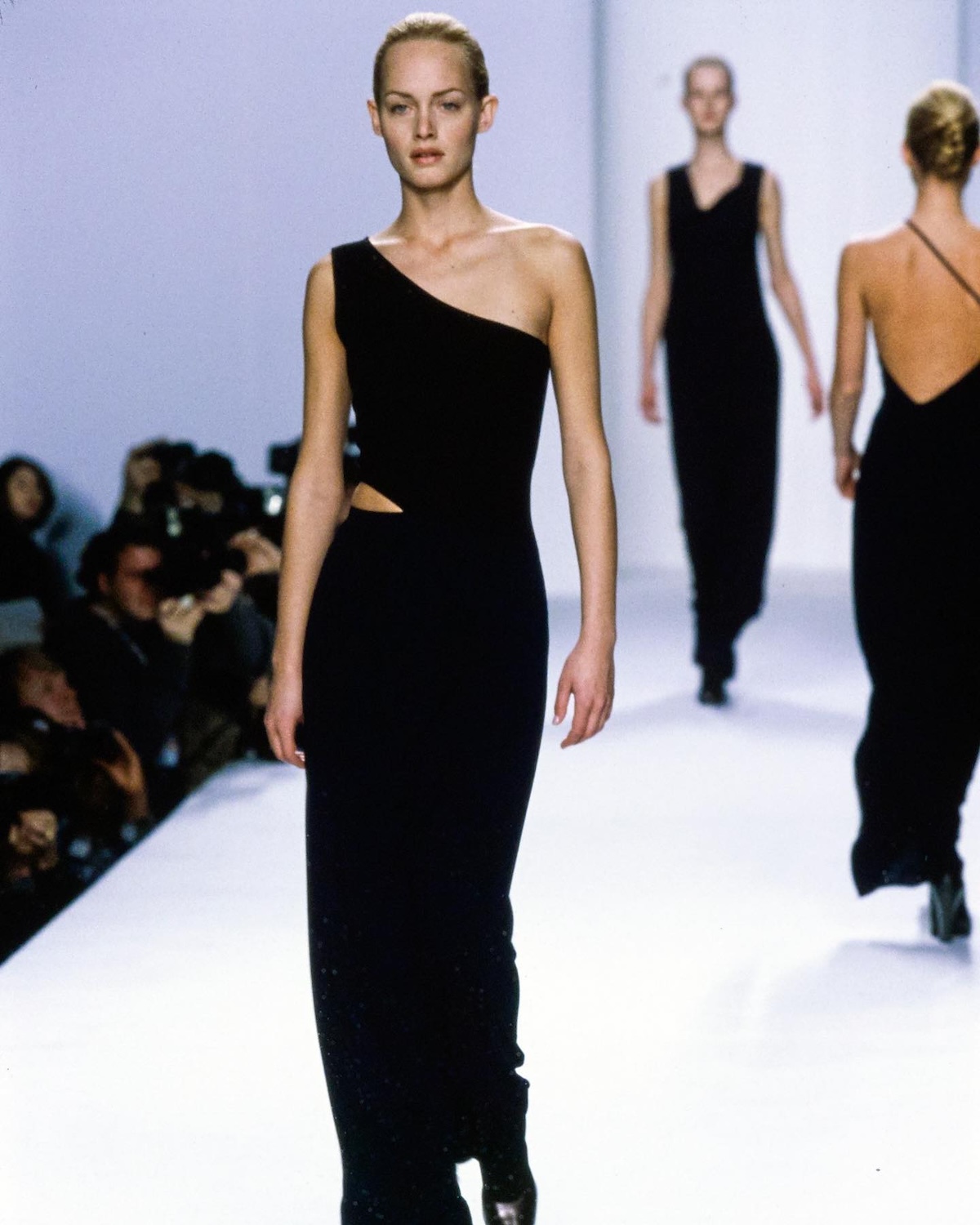 La modelo Amber Valletta desfila con un vestido negro asimétrico de un solo hombro en la colección Otoño/Invierno 1996 de Calvin Klein Collection